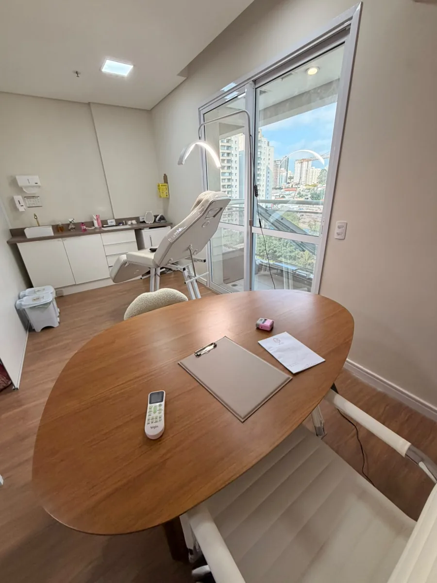 Sala de atendimento com mesa oval de madeira, poltrona e vista da cidade